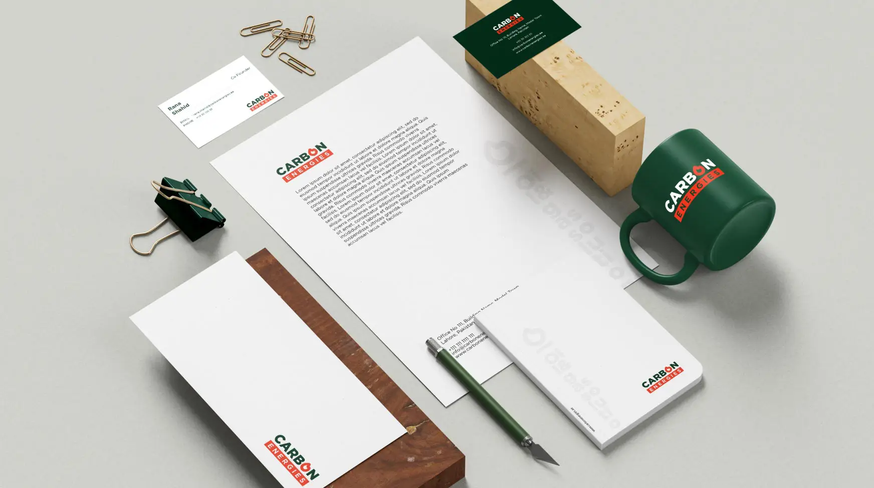 This image showcases a brand identity mockup for Carbon Energies, an engineering company in the oil, gas, and energy sector. Carbon Energies, a multidisciplinary engineering firm based in Lahore, Pakistan. The mockup features corporate stationery including business cards, a letterhead, an envelope, and a branded mug. The design utilizes a minimalist aesthetic with a dark green and red color palette.